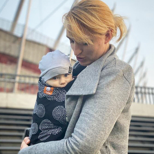 A woman holding a baby outside near a stadium.