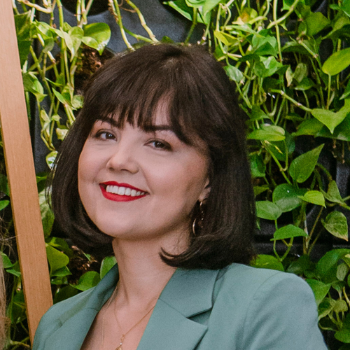 Weronika, preschool owner, smiling in front of a green plant wall.