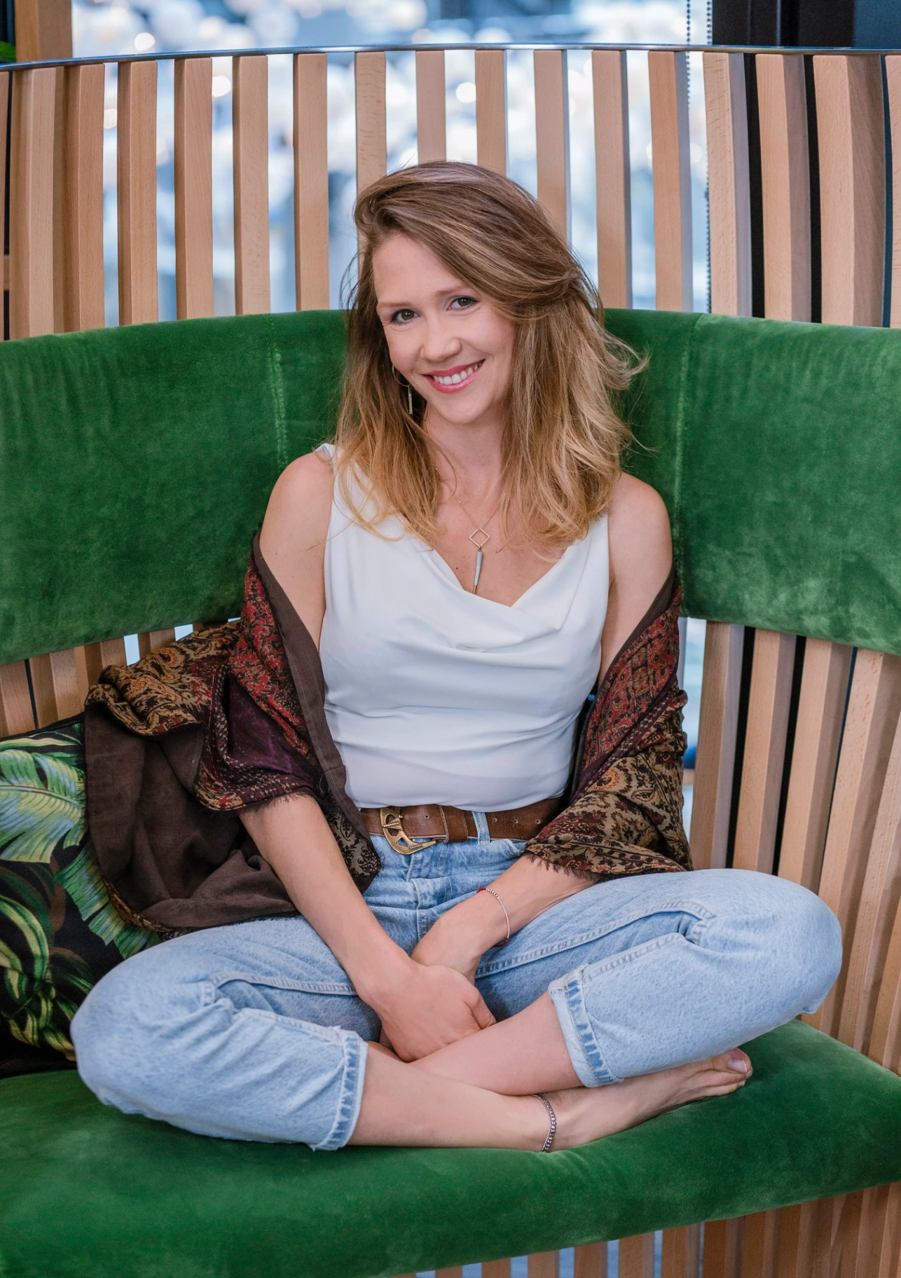 Alex Kozera, founder of BLISKO, sitting cross-legged on a green velvet seat.